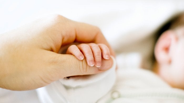 Newborn holding mothers thumb.