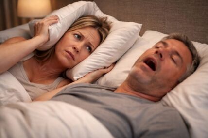 Man snoring loudly, while wife muffles sound with pillow.