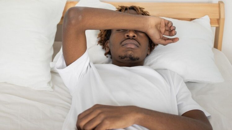 A man lying down and covering their eyes in bed.