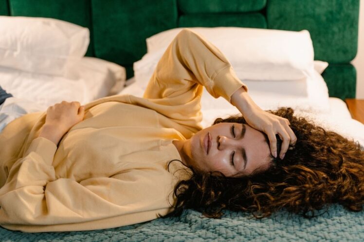 A woman lying down in bed holding her head.